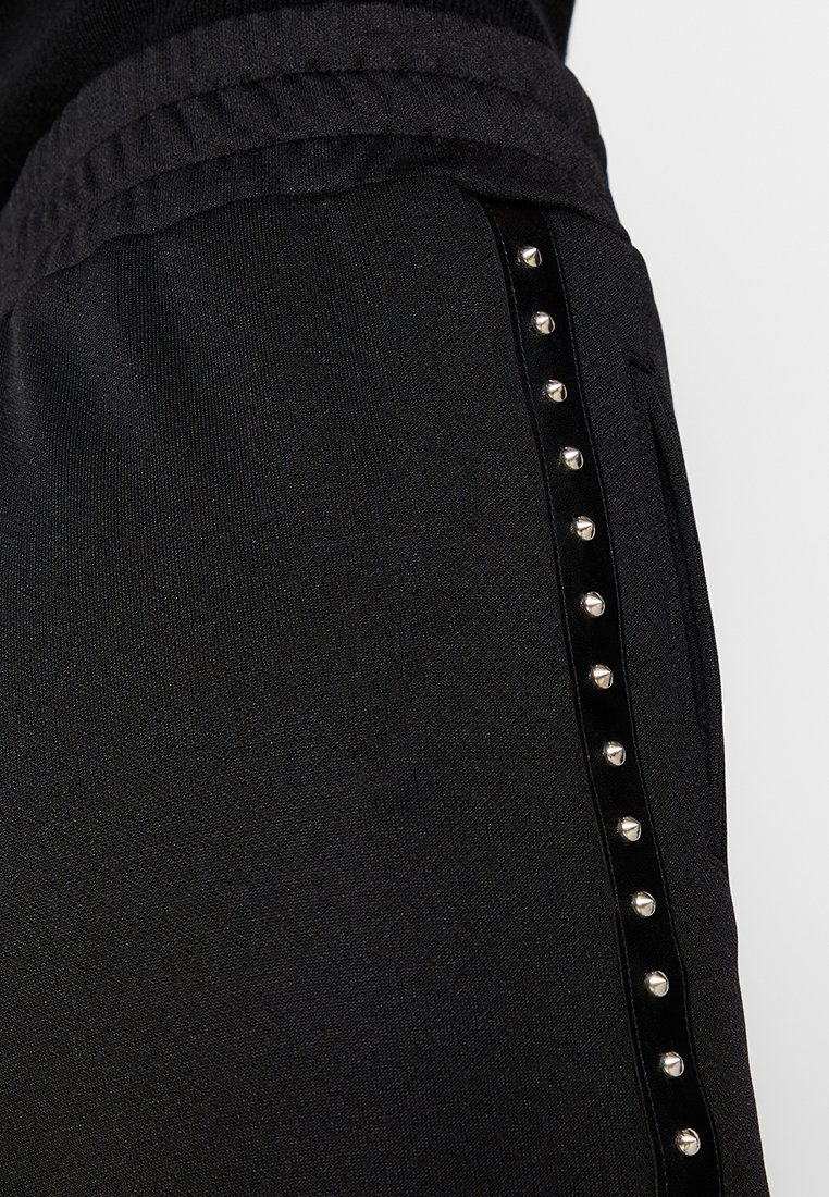 Pantaloni jogger neri in tessuto testurizzato con una cintura elastica, dotati di un pannello laterale decorato con borchie rotonde in metallo argentato.