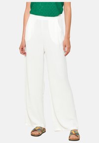 Weiße, fließende weit geschnittene Hosen aus leichtem Material. Verfügt über Vordertaschen und einen hohen Taillenbund. Die Schuhe sind bunt und mit Mustern versehen.