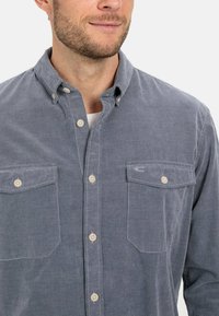 Hellblaues Cordhemd mit Button-Down-Kragen, zwei Brusttaschen und kleinen sandfarbenen Knöpfen. Das Hemd zeichnet sich durch eine strukturierte Oberfläche und ein dezentes Muster aus.