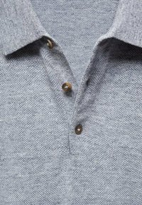 Polo shirt tricoté gris avec un tissu texturé, doté d'un col et de trois boutons marron sur le devant. Design décontracté.