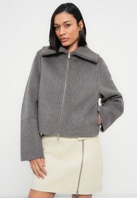 Γκρι μάλλινο μπουφάν με φερμουάρ, ευρύ ριμπ πλάγιο γιακά και κοντά μανίκια. Υφασμένο ύφασμα με λεία επιφάνεια, συνδυασμένο με κρεμ φούστα.