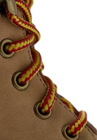 Bota de cuero marrón con cordones trenzados rojos y amarillos, ojales de metal y una superficie texturizada. Primer plano del detalle de los cordones y la parte superior de la bota.
