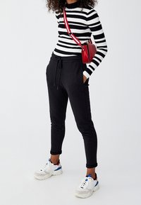 Sorte jogger-bukser med elastisk talje, parret med en tætsiddende langærmet top i sort og hvid striber og hvide sneakers. Rød taske båret crossbody.