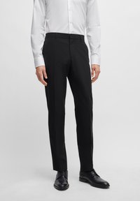 Black tailored trousers with a flat front design, made from a smooth fabric. Worn with a white shirt and black shoes.