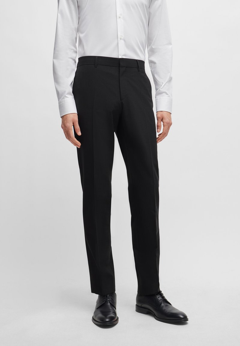 Black tailored trousers with a flat front design, made from a smooth fabric. Worn with a white shirt and black shoes.