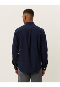 Camicia blu navy con bottoni in cotone, caratterizzata da un colletto a punta, maniche lunghe e spacco laterale all'orlo per facilitare i movimenti.