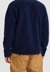 Marinkolad fleecetröja med strukturerad yta, långa ärmar och avslappnad passform, ihop med ljusbruna cargobyxor med bakfickor.