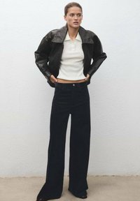 Črna usnjena kraj�šana jakna preko bele rebraste polo majice, v paru z visokim pasom in širokimi temnimi kavbojkami. Minimalističen dizajn.