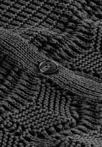 Gros plan d’un tissu tricoté noir avec des motifs texturés et un bouton noir à quatre trous cousu dessus.