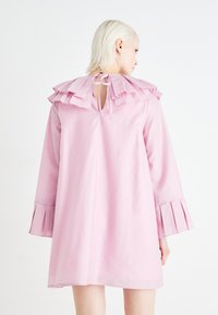 Ροδοκόκκινο φόρεμα με ριχτό κολάρο και κ�λείσιμο με κορδόνι στο πίσω μέρος, με μακριά μανίκια που έχουν πλισέ λεπτομέρειες στις μανσέτες. Λείο ύφασμα.