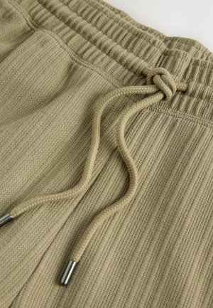 Pantaloni jogger color khaki realizzati in tessuto testurizzato, con vita elasticizzata, coulisse regolabile e dettagli in metallo argentato.