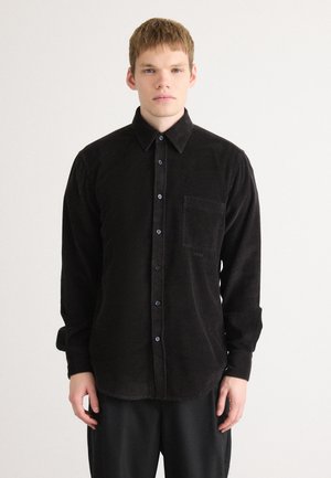 Black corduroy shirt with long sleeves, front pocket, and button-down closure. Features a textured surface and dark blue buttons.