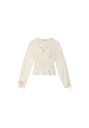 Crèmekleurige blouse met lange mouwen, een gerimpelde taille, V-halslijn, gerafelde kraag en roze lintstrikjes aan de mouwboorden.