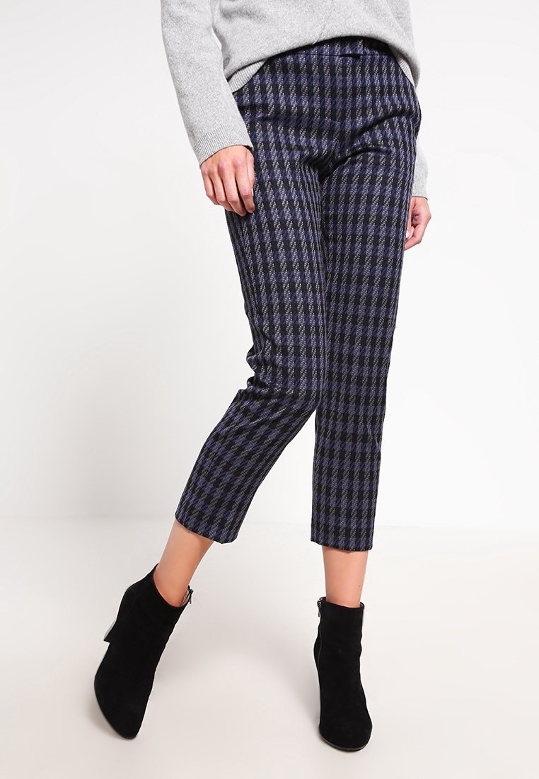 Un pantalon à carreaux bleu marine et noir, à coupe slim, longueur raccourcie, avec une texture subtile, associé à des bottines noires.