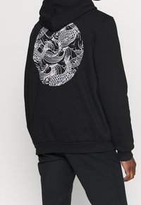 Felpa con cappuccio nera in cotone con un grande disegno di un pesce bianco sul retro, maniche lunghe e cappuccio. Tessuto liscio e vestibilità comoda.