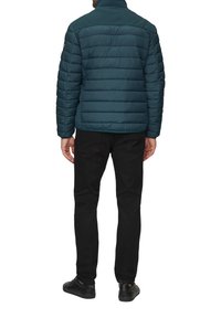 Tealen pufferjack met verticale gestikte ontwerp, hoge kraag en zwarte jeans. Draag het met zwarte sneakers, gezien vanuit de rug.