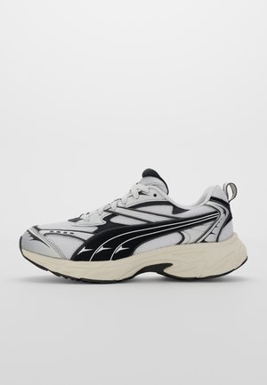 Chaussure de sport texturée blanche et noire avec une tige en maille, semelle rembourrée et profils latéraux distincts offrant des lignes courbées et des accents.
