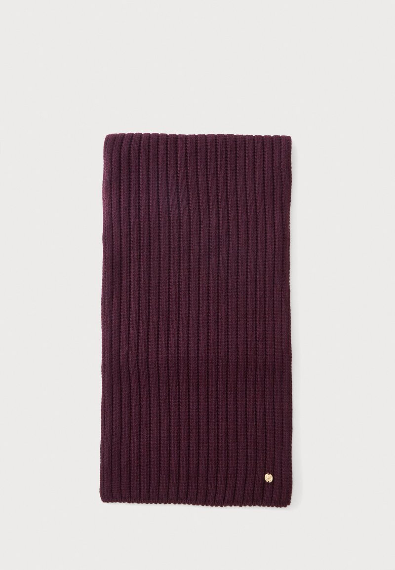 Écharpe en tricot côtelé violet foncé pliée avec un petit emblème doré rond près d'un bord sur un fond clair.