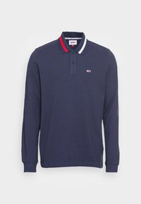 Námořnicky modrá polo košile s dlouhým rukávem, s límcem v červené, bílé a modré pruhované barvě a malým logem Tommy Jeans na hrudi.