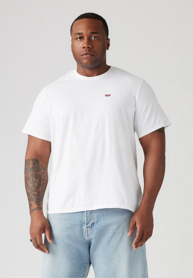 Witte katoenen t-shirt met een ronde hals, korte mouwen, met een klein rood logo op de borst. Gecombineerd met lichtblauwe jeans.