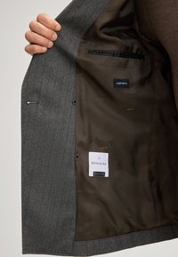 Blazer grigio a righe in lana con interno in satin marrone, dotato di due bottoni e etichette che indicano il tipo di tessuto e il marchio. Foderato con materiale morbido.