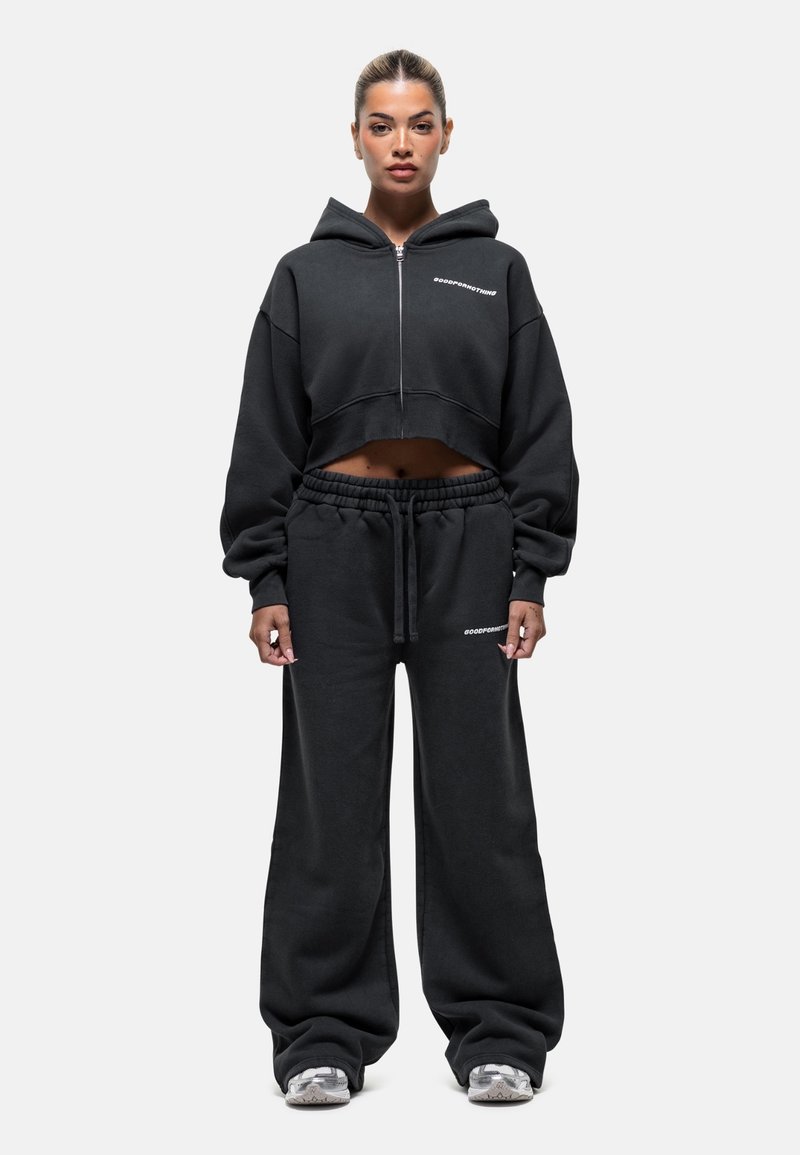 Zwarte cropped hoodie met rits, wijde mouwen en logo-detail, gecombineerd met losse zwarte sweatpants met elastische taille en logo-acenten.