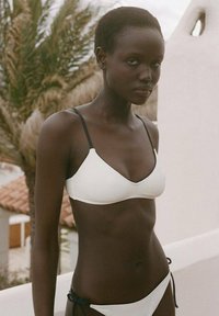 Bikini set featuring a white triangular bralette and matching bottom with black straps. Smooth texture and minimalistic design.