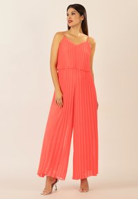 Mono coral plisado con tirantes finos y escote en V, que presenta un corte holgado y piernas anchas, complementado con acentos metálicos.