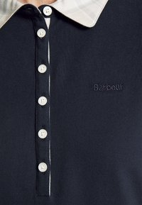 Polo bleu marine avec des boutons blancs, un col beige et "Barbour" brodé sur la poitrine.