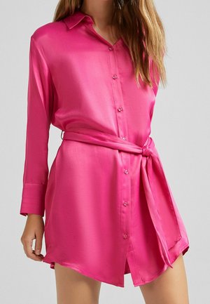 Robe chemise en satin rose avec des manches longues, un col, une fermeture à boutons et une ceinture assortie. Présente une texture lisse et des fentes sur les côtés.