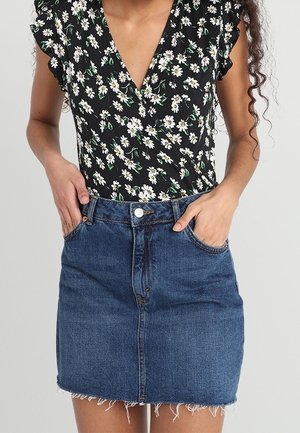 Haut noir style cache-cœur avec motif floral blanc ; mini-jupe en denim avec ourlet effiloché, bouton frontal et deux poches latérales.