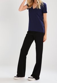 Marinblå t-shirt med v-hals som matchas med svarta raka byxor och svartvitt sneakers. Slät tyg, avslappnad passform, avslappnad design.