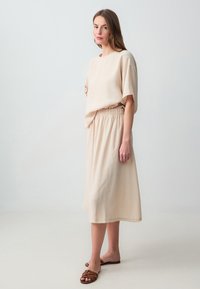 Haut beige à manches courtes avec une coupe décontractée, associé à une jupe midi assortie. La jupe a une taille élastique et une texture douce.