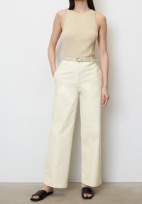 Beige ribbet tanktop parret med højttaljede, brede cremede bukser sikret med et bælte. Sorte slidesandaler fuldender outfittet.