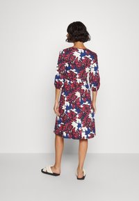Vestido floral con un fondo azul marino, que presenta grandes flores blancas y rojas. Mangas tres cuartos, hasta la rodilla, diseño de corte relajado.