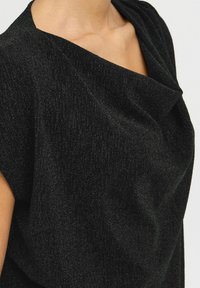 Top nero in tessuto testurizzato con sottili fili metallici. Presenta una scollatura drappeggiata e maniche corte, evidenziando una vestibilità comoda.