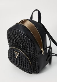 Sac à dos en cuir noir avec une texture tissée, deux compartiments zippés et des finitions en doré. L'intérieur est doté d'une doublure neutre avec un motif de logo.