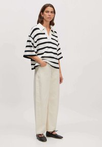 Zwart-wit gestreepte gebreide poloshirt met V-hals, gecombineerd met crèmekleurige wijde broekspijpen. Zwarte platte schoenen maken de look compleet.
