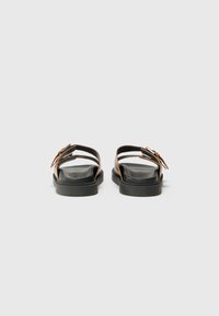 Sandale din piele maro, cu două curele reglabile, o talpă căptușită neagră și o talpă groasă din cauciuc negru. Design minimalist.