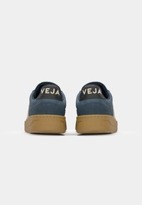 Sneaker blu in pelle scamosciata con suola in gomma marrone, dotate di tacchi neri con l'etichetta "VEJA" in bianco. Design semplice con accenti minimali.