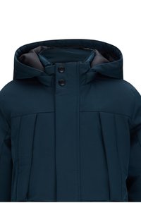 Giacca imbottita di un verde scuro con colletto alto, grande cappuccio e due bottoni a pressione sul davanti. Tessuto texturizzato con pieghe ricamate.