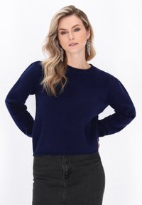 Marineblauer Strickpullover mit langen Ärmeln und Rundhalsausschnitt. Mit leicht gepufften Ärmeln und weichem Material, kombiniert mit einem schwarzen Rock.
