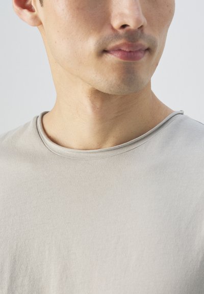 Harmaa t-paita, joka on valmistettu pehmeästä kankaasta, jossa on sileä pinta. Paitassa on pyöreä kaula-aukko ja lyhyet hihat. Yksinkertainen, minimalistinen muotoilu.