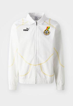 Balta užtrauktuku užsegama striukė su geltonais geometriniais siūlėlėmis. Kairėje krūtinės pusėje - Puma logotipas ir Ganos futbolo asociacijos emblema. Elastinės rankogalių apkaustai.