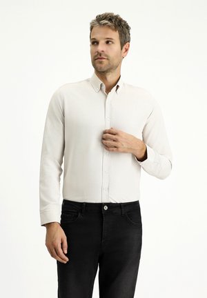 Helle beige Hemdbluse mit strukturiertem Stoff, langen Ärmeln und Kragen, kombiniert mit dunklen Jeans. Einfaches, minimalistisches Design.