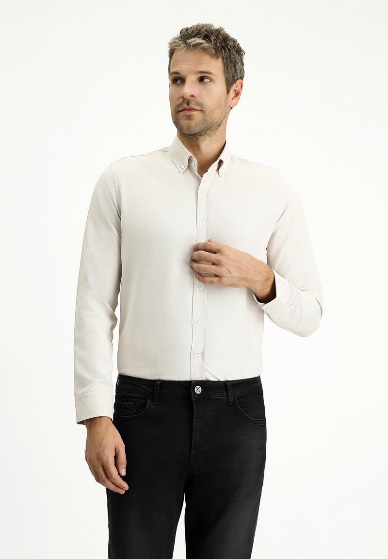 Camicia button-up beige chiaro con tessuto texturizzato, maniche lunghe e colletto, abbinata a jeans scuri. Design semplice e minimalista.