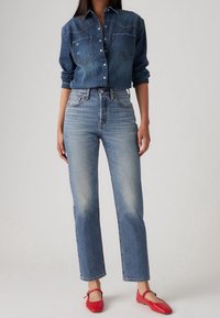 Camisa vaquera con dos bolsillos en el pecho, diseño abotonado y color azul ligeramente desgastado. Vaqueros azules estándar con corte recto y acabado descolorido. Bailarinas rojas.