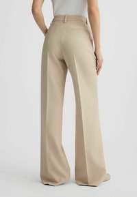 Pantaloni beige a gamba larga con una finitura in tessuto liscia, caratterizzati da cuciture posteriori, due tasche e una vita sagomata.
