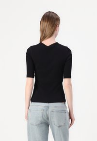 Sort kortærmet top med en tætsiddende pasform og V-udskæring, lavet af ribbet strikstof. Bæres med lyseblå jeans.