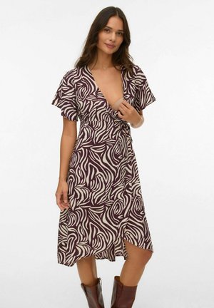 Brūna un krēmbalta rakstainā kleita ar īsām piedurknēm, dziļu V veida kakla izgriezumu, piegulošu vidukli un asimetrisku apakšmalu, apvienota ar brūnām zābakiem.